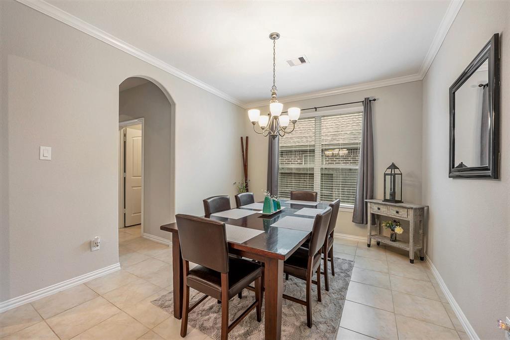 A neatly arranged dining room with a dark wood table, six chairs, chandelier, window with curtains, and minimalistic decor.