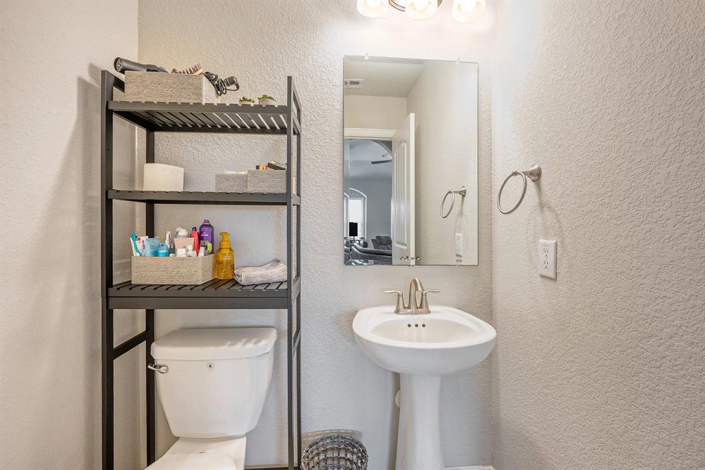 A small bathroom with a white pedestal sink, toilet, mirror, and a black shelving unit with toiletries and towels.