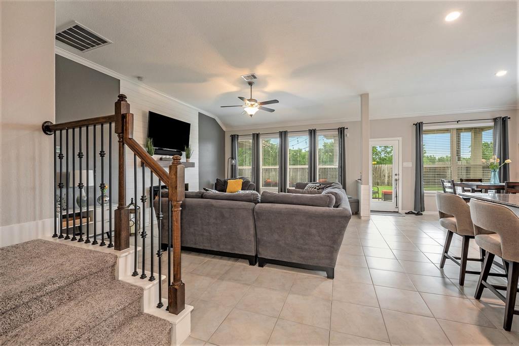 Modern living room with sectional sofa, staircase, tile flooring, dining area, and sliding doors leading to a backyard.