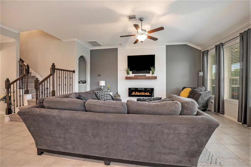 A modern living room with a large grey sofa, fireplace, mounted TV, and staircase leading to an upper level.