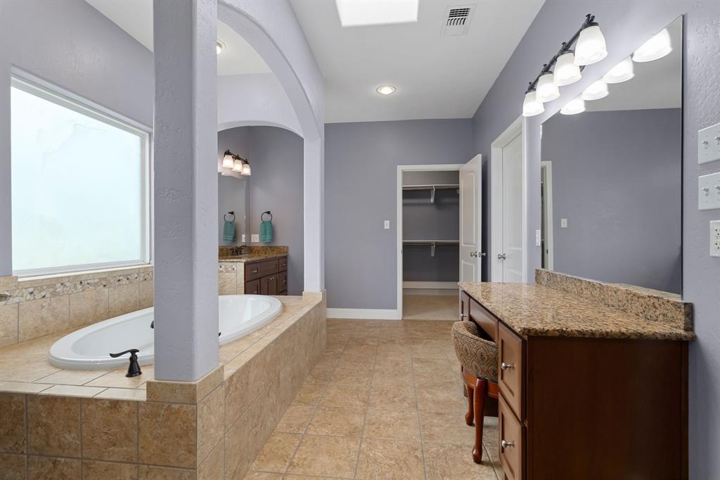 Primary bathroom with granite countertops, tiled flooring, dual sinks, individual vanity w/ it\'s own mirror, walk in shower and separate bathtub.