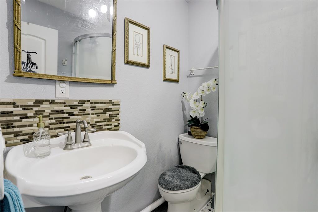 A small bathroom with a pedestal sink, decorative backsplash, mirror and a shower stall.