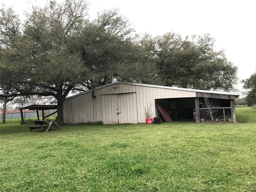 Mmetal shed, carport, picnic table, and trees on a grassy field.