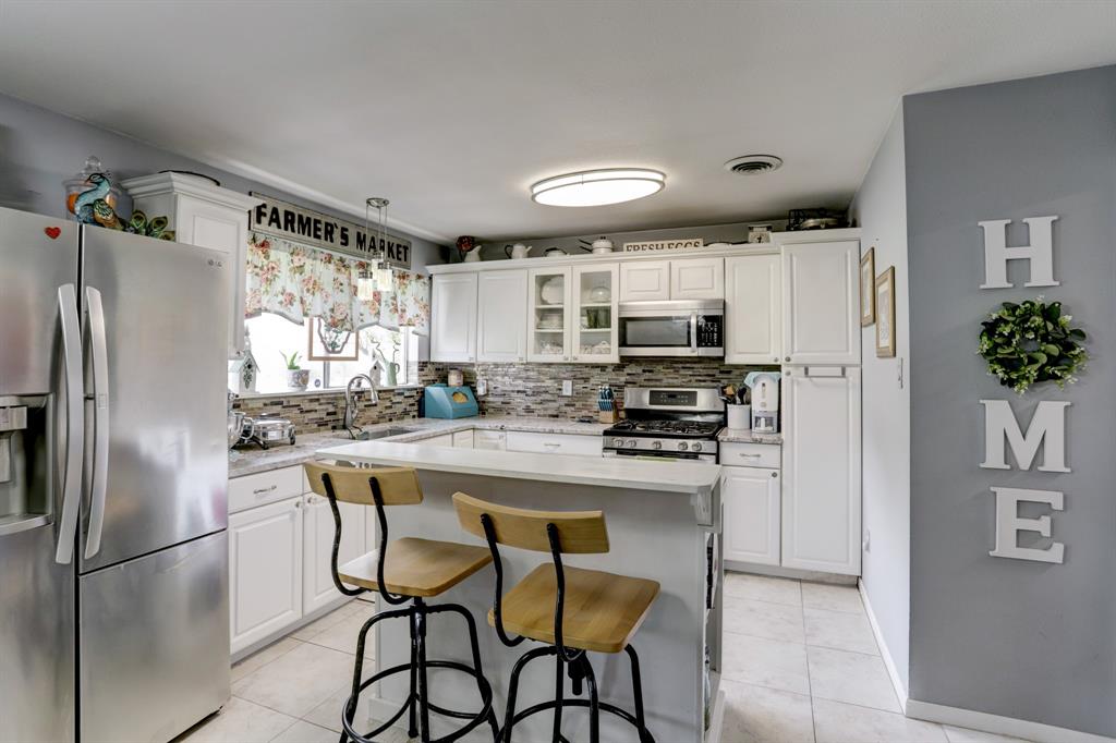 Modern kitchen interior with white cabinets, stainless steel appliances, and a central island with stools.