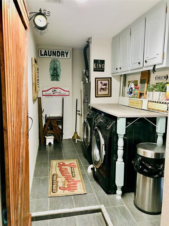 A cozy, narrow laundry room with white cabinets, a front-loading washer and a wooden countertop.