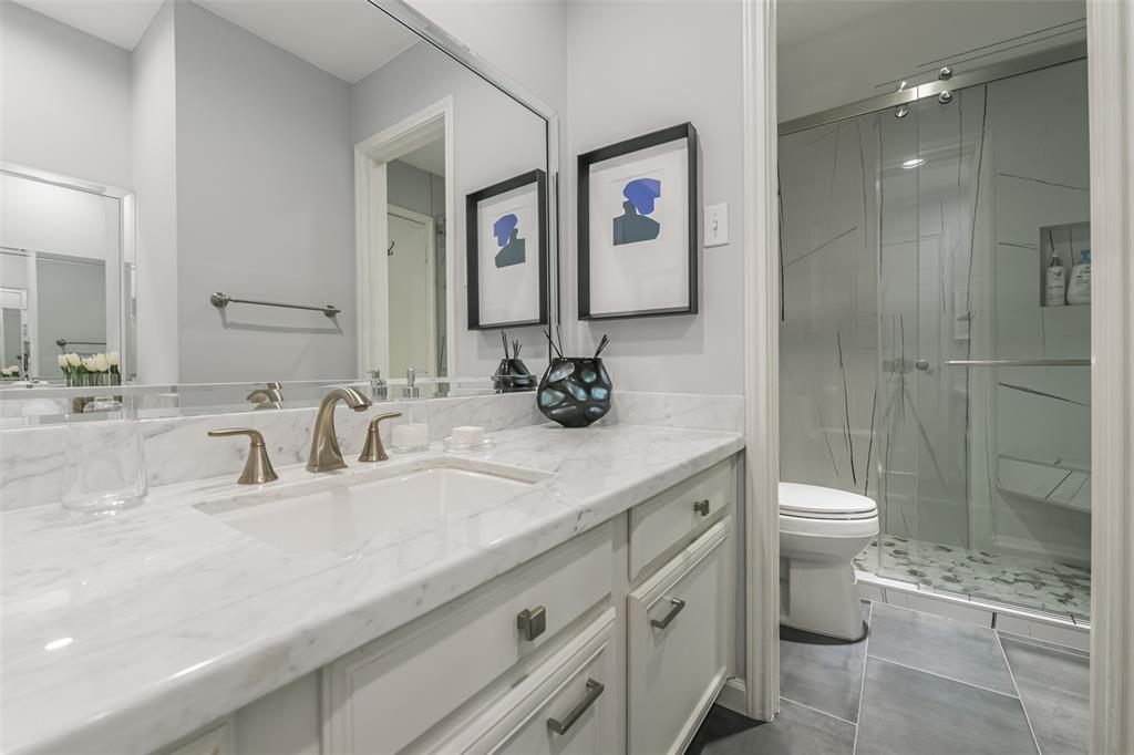 Flawlessly updated secondary bath provides marble counters and a beautifully tiled walk-in shower.  The built-in marble topped vanity is reflected in the mirror.