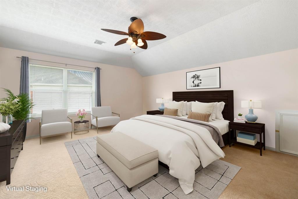 Secondary bedroom features plush carpet, custom paint, dark stained ceiling fan with lighting, space for a seating area and a large window with privacy blinds.