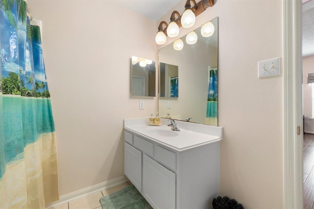 Secondary bathroom features light countertops and cabinets, neutral paint, shower/tub combo, large mirror, tile floors, sleek fixtures and overhead lighting.