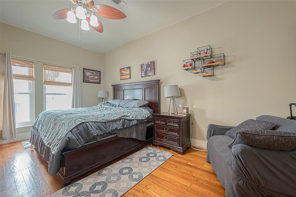 The upstairs primary bedroom features large windows, a ceiling fan and hardwood flooring.