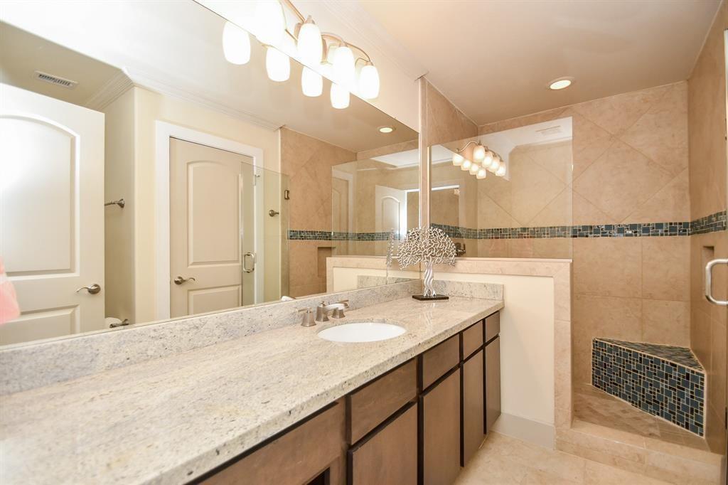 Delicate lighting above a wall-wide mirror gives even greater visual space in this welcoming bath. Luscious granite (?) countertops and adobe tinted, tiled shower with glass shield, makes this an accommodating space for relaxation.