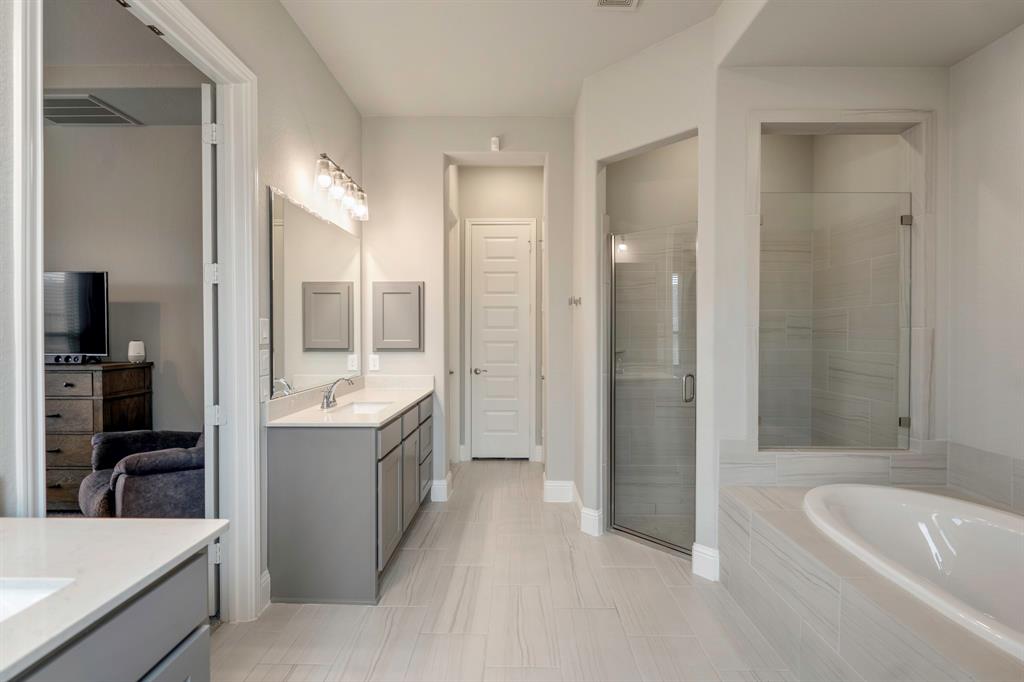 The primary bathroom offers a walk-in shower with tile surround, glass door and window for additional lighting, mud set floors, and sleek gray tile, plus a large garden tub.