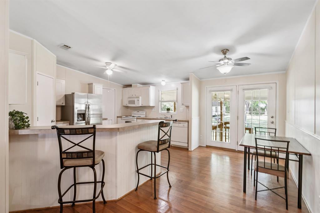 The living area opens to a kitchen area featuring white cabinetry, modern appliances, bar seating, and ample natural light from the glass doors.