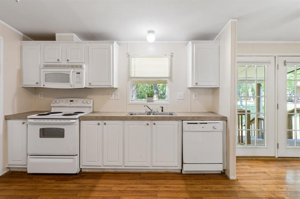 Bright kitchen with lots of cabinets, white appliances, hardwood look floor, and double doors leading to a deck. Neutral colors, clean, and well-lit space.