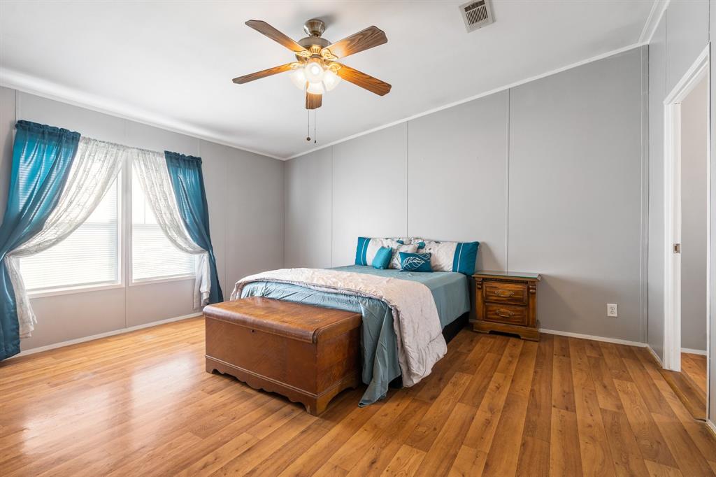 The primary bedroom features hardwood floors, a ceiling fan, large windows with blue curtains, and a matching bedspread and pillows.