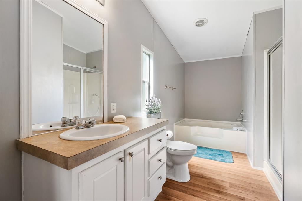 Primary bathroom with wooden floors, white cabinetry, dual sink vanity, large mirror, bathtub and seperate shower. Neutral tones, clean, and bright.