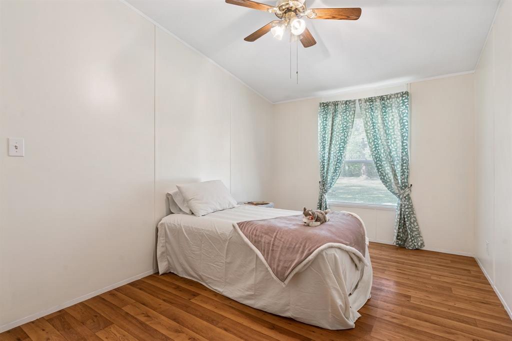 The 3rd bedroom has a simple bed with white bedding, wood floors, a ceiling fan, and patterned curtains flanking a window with natural light.