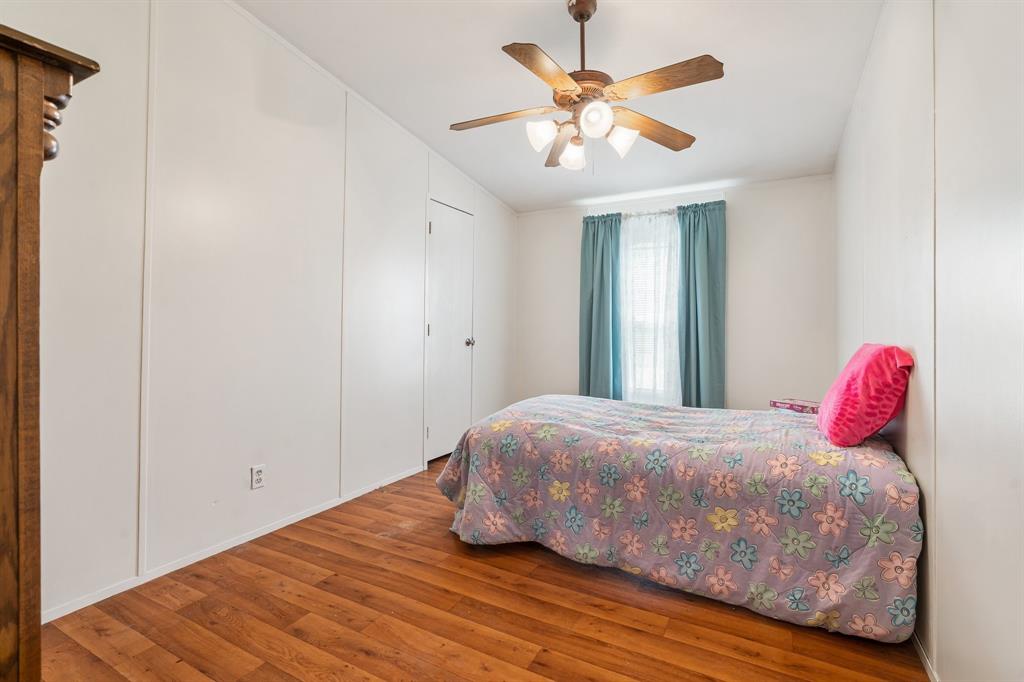 The 2nd bedroom features hardwood floors, a single bed with floral bedding, a ceiling fan, built-in closet, and teal curtains over a window.