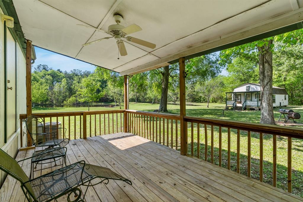 Back porch memories of tranquil afternoons, a wooden deck with chairs overlooking a lush yard, trees, and a quaint guest house basking in serene sunlight.