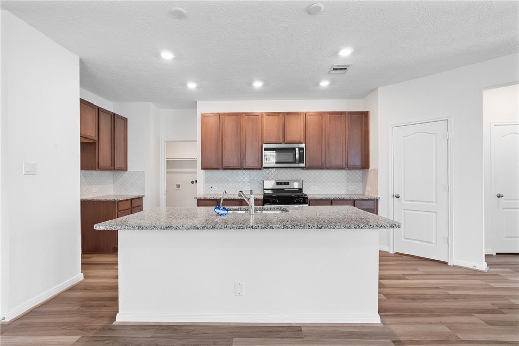 This spacious kitchen features high ceilings, stained wood cabinets, granite countertops, SS appliances, modern tile backsplash, recessed lighting, extended counter space, granite kitchen island with double sink and space for breakfast bar, and a walk-in pantry all overlooking your huge family room!