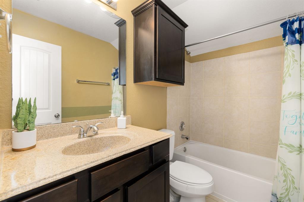 Secondary bath features tile flooring, bath/shower combo with tile surround, dark wood cabinets, granite countertops, mirror, dark and sleek features.