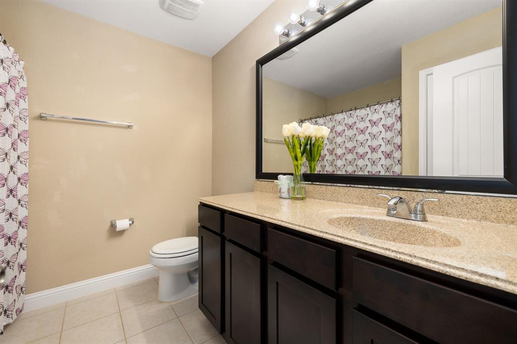 Secondary bath features tile flooring, bath/shower combo with tile surround, dark wood cabinets, granite countertops, mirror, dark and sleek features.