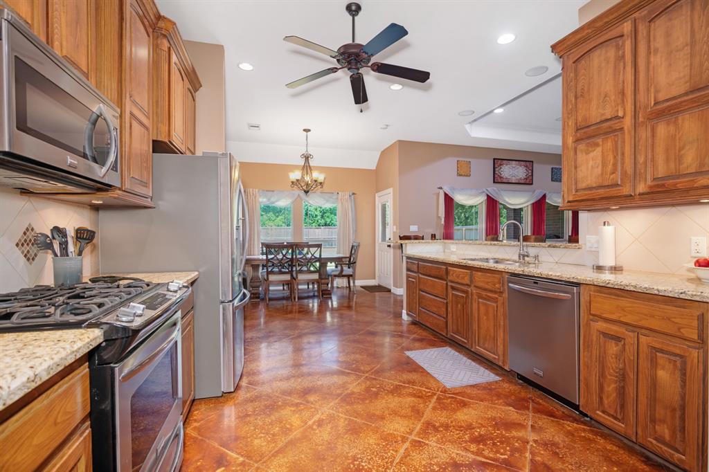 Spacious kitchen with wooden cabinets and granite countertops, leading to a dining area with a view of the outside.