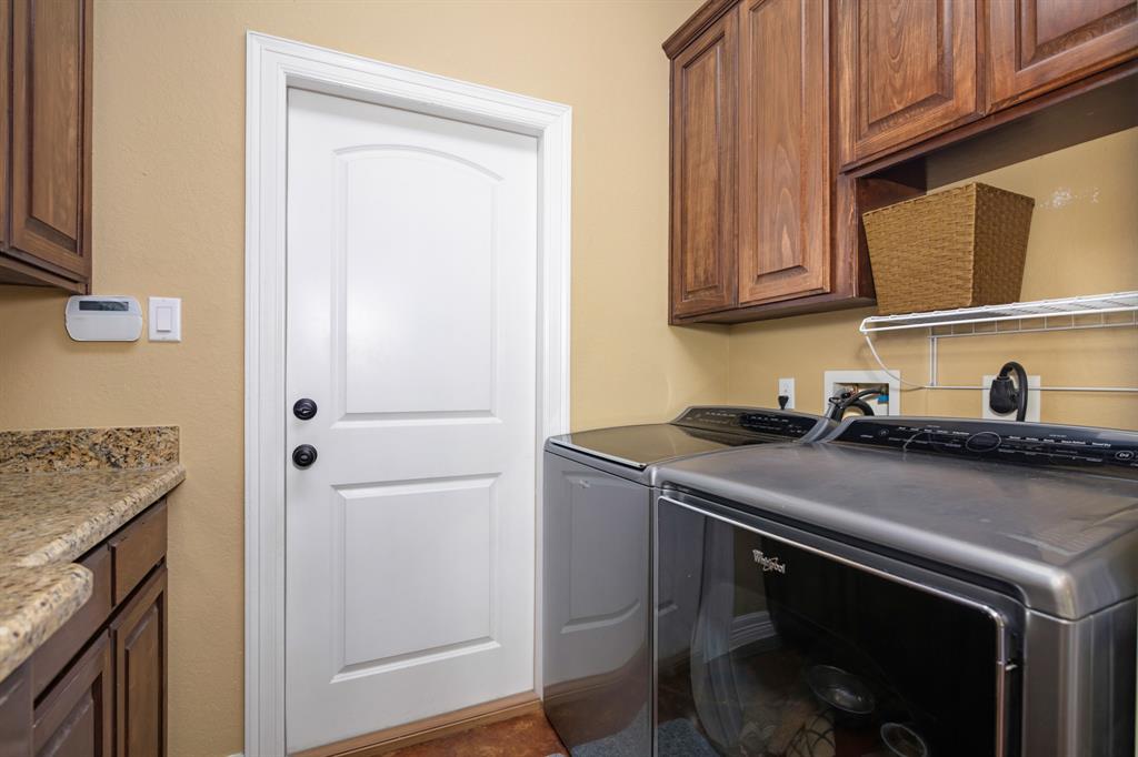 Modern laundry room with washer, dryer, wooden cabinets, granite countertop, and a door leading to the garage