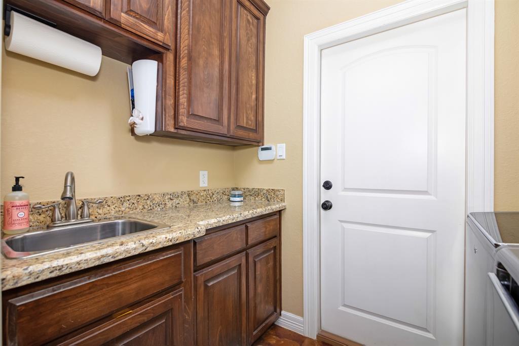 Utility room with a stainless steel sink, wooden cabinets, and granite countertop.