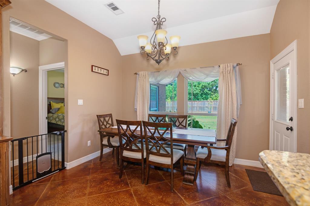 Spacious dining room with a six-seater table, tiled floor, chandelier, and a view of the fenced backyard through windows.