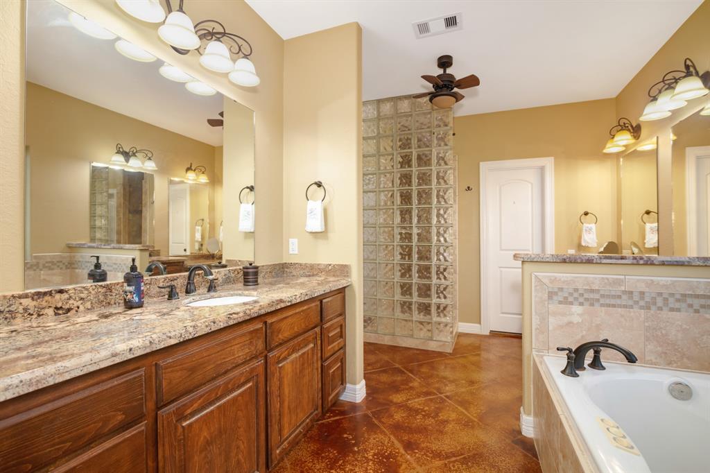 Spacious bathroom with dual vanities, large mirror, walk in tiled shower, whirlpool tub, and warm color tones.