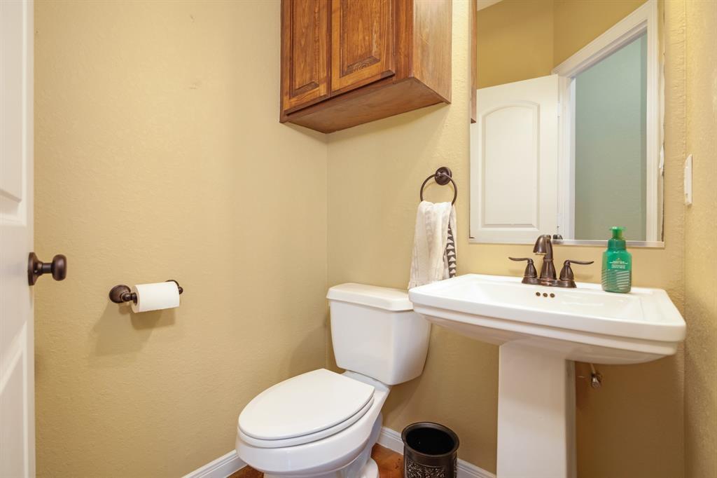 Small guest bathroom with toilet and pedestal sink, warmly lit with beige walls.