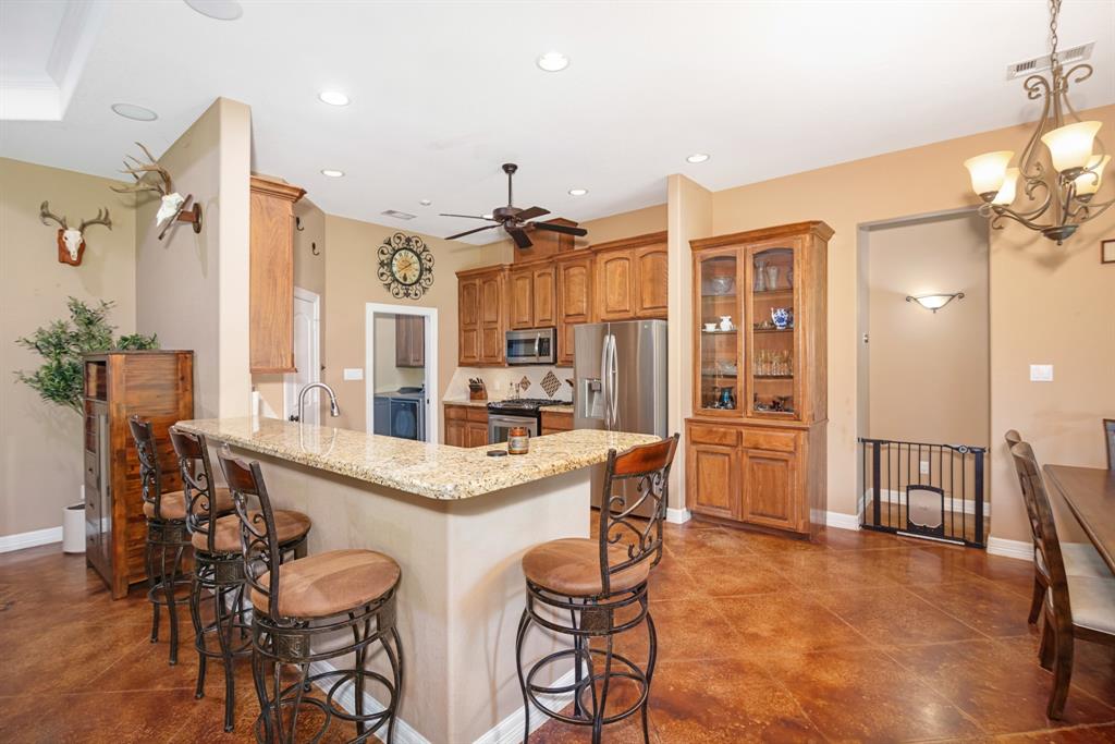 Spacious kitchen, island bar with stools, wooden cabinets, stainless steel appliances, and decorative lighting.