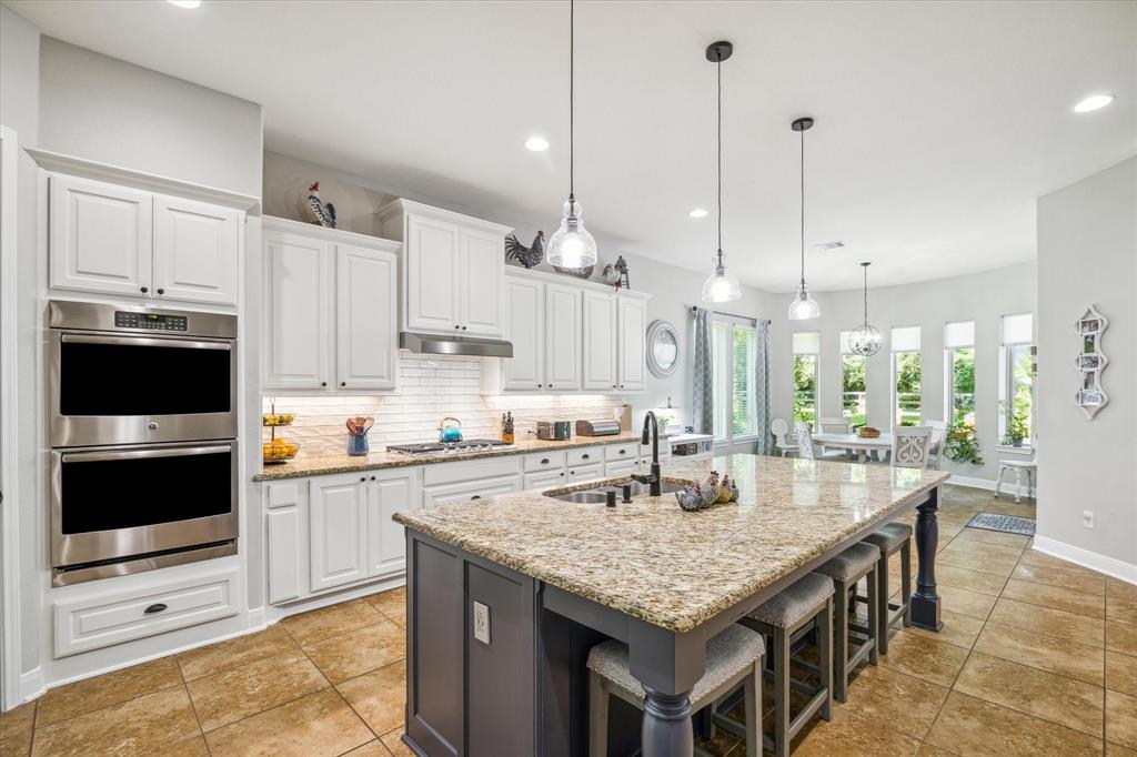 Modern kitchen with white cabinets, granite countertops, stainless steel appliances, pendant lights, and a view of an adjoining dining area.