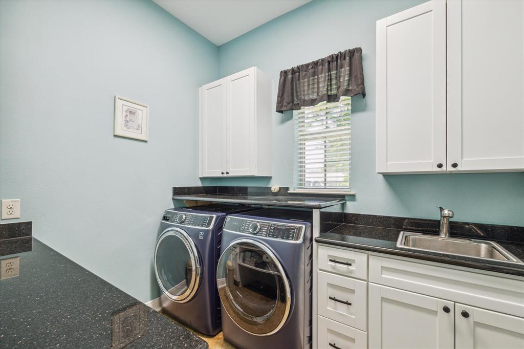 Laundry room with a washer, dryer, white cabinetry, black countertops.