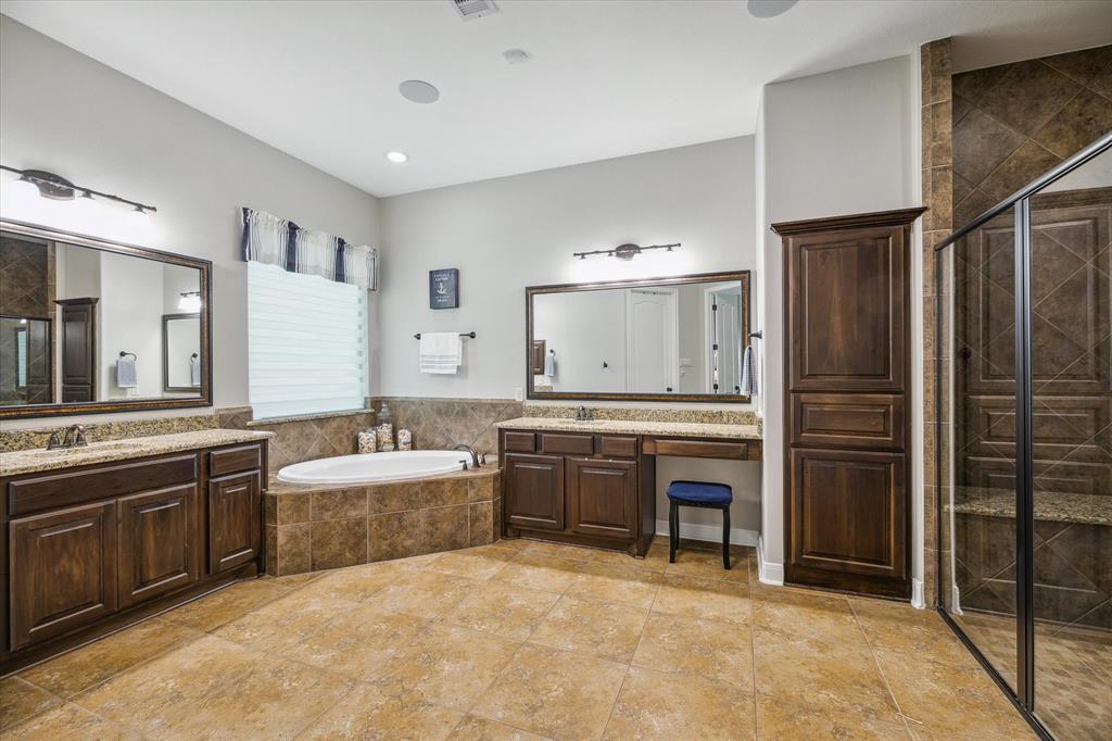 A spacious bathroom with dual vanities, large mirrors, a garden tub, tiled flooring, and a large glass-enclosed shower.