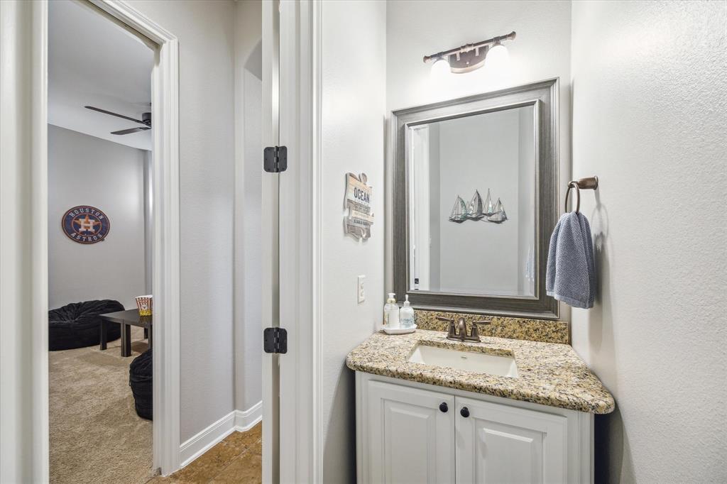 A 1/2 bathroom with a granite countertop sink, mirror, and a view into the 1st floor media room.