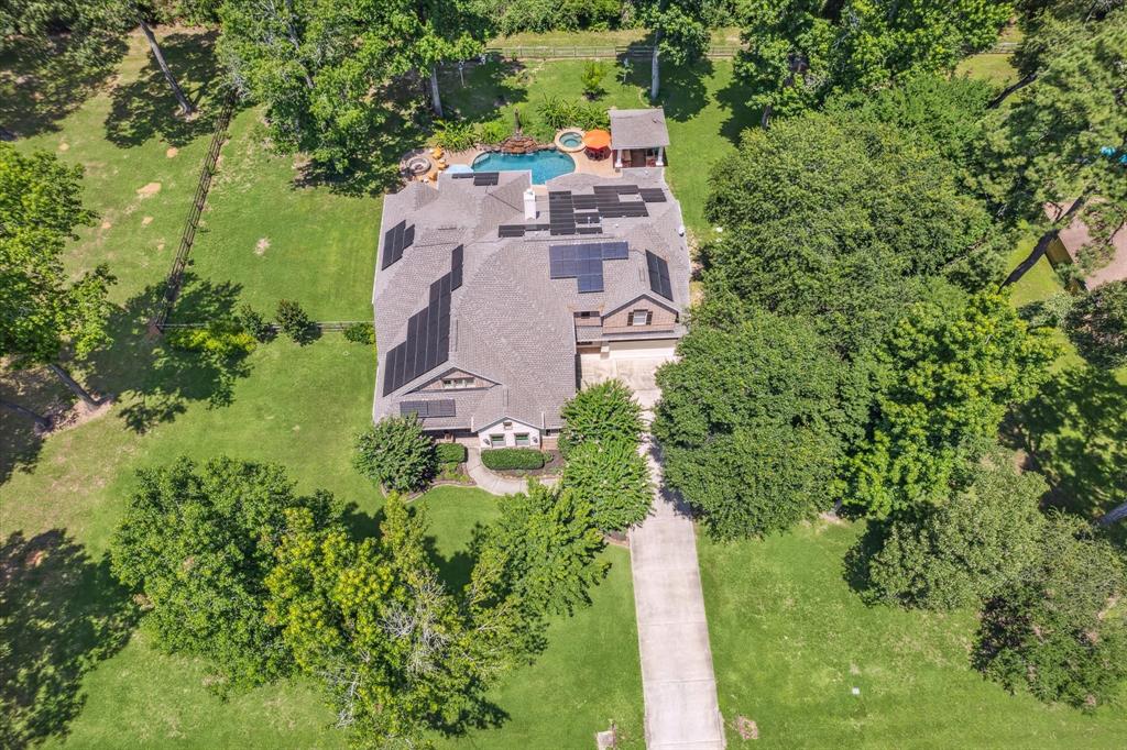 Aerial view of a large house with solar panels, a swimming pool, surrounded by trees and a well-manicured lawn.   Behind the home is a wooded area which is landlocked and to the left of the home is a lot owned by the neighbor