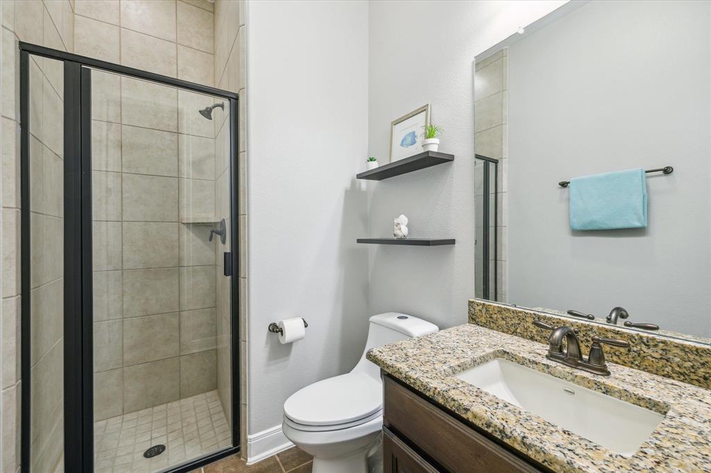 Modern bathroom with a glass shower, granite countertop sink, toilet, and minimal decor on floating shelves.