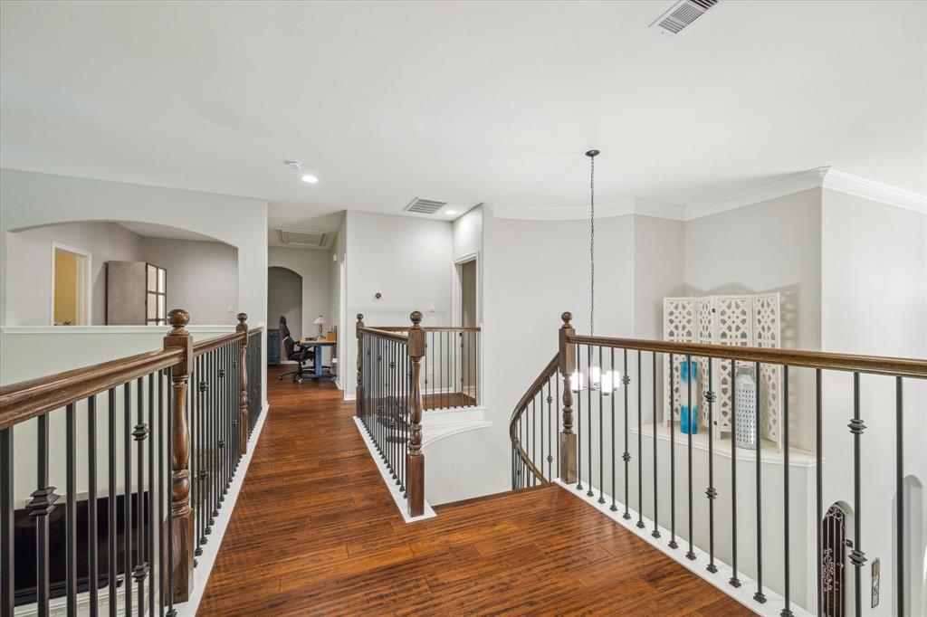 Spacious, well-lit hallway with wooden floors, and dark iron balustrades overlooking an interior space.