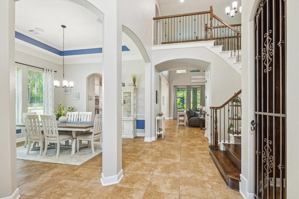 Elegant house interior with high ceilings, archways, a wooden staircase, iron banister, dining area, and tiled floors, showcasing a spacious and luxurious design.