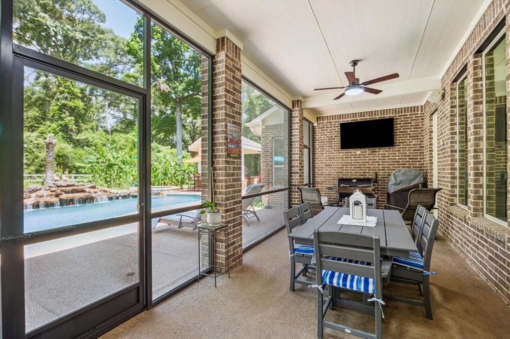 Screened in covered patio with ceiling fan and TV, overlooking pool with a rock waterfall surrounded by trees.