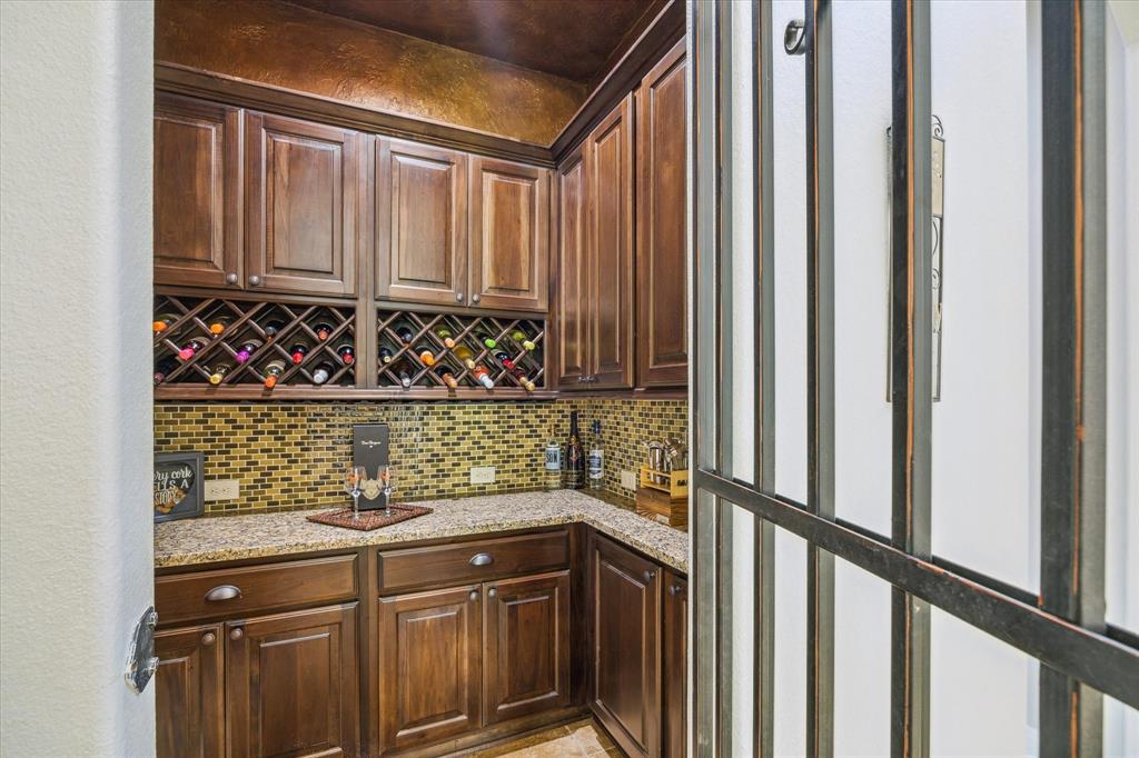 Wine grotto, mosaic backsplash, and granite countertops, viewed through a wrought iron door