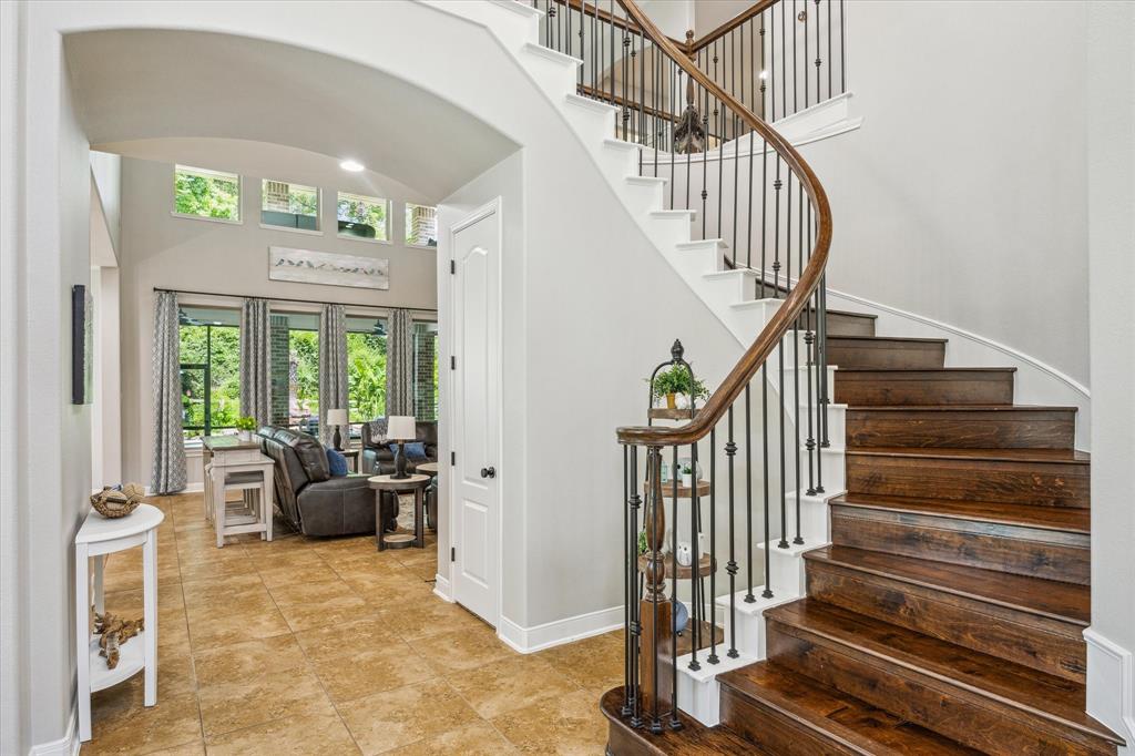 Elegant interior entryway with curved staircase, hardwood steps, iron balustrades, high ceilings, and natural light throughout the home