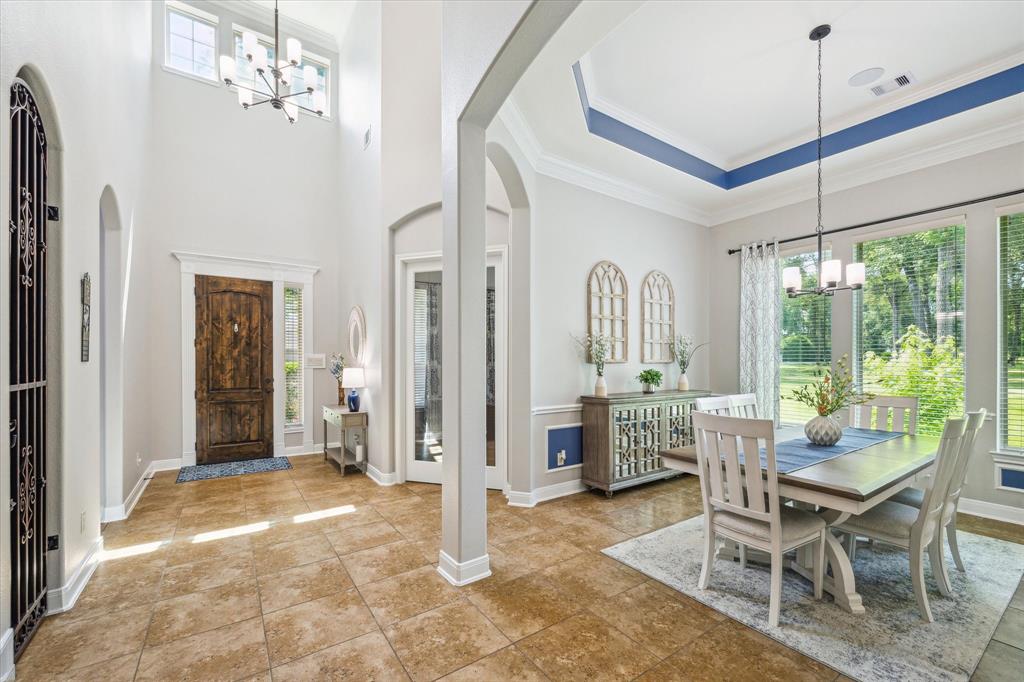 A bright, elegant formal dining area with tray ceiling, large windows, adjacent entryway to the kitchen.