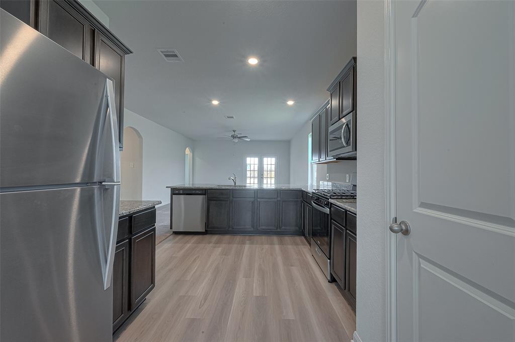 Modern kitchen interior with stainless steel appliances, dark cabinetry, and light wood flooring, leading to a bright, open living space.