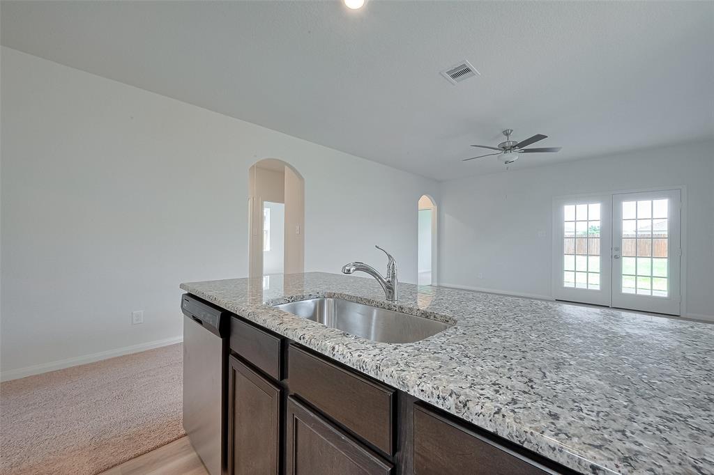 Modern kitchen with granite countertops, dark cabinets, and a view into a bright room with a ceiling fan and French doors leading outside.