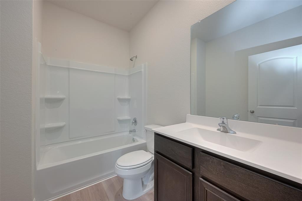 A clean, modern bathroom with a white tub/shower combo, toilet, and vanity with a sink and mirror. Bright and minimalistic design.