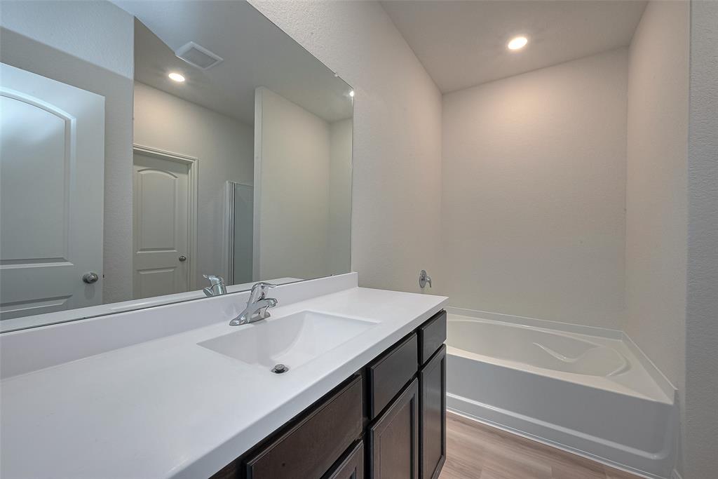 Modern bathroom with a large mirror, white countertop, under-mount sink, dark cabinets, and a built-in bathtub. Neat and well-lit interior.