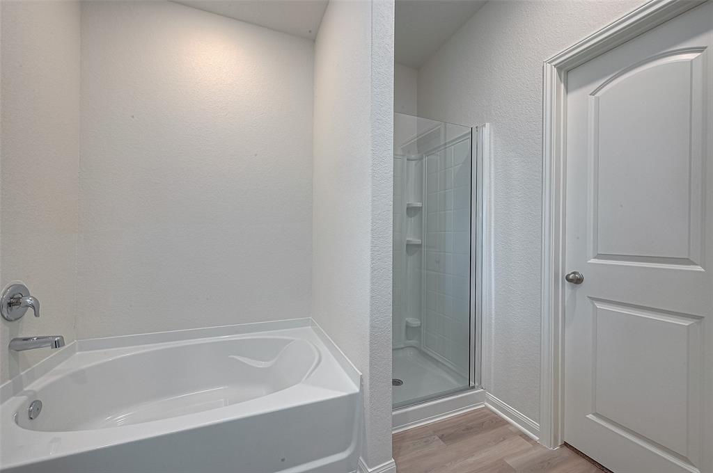 Modern bathroom corner with a white bathtub and a separate glass-enclosed shower, featuring neutral tones and clean lines.