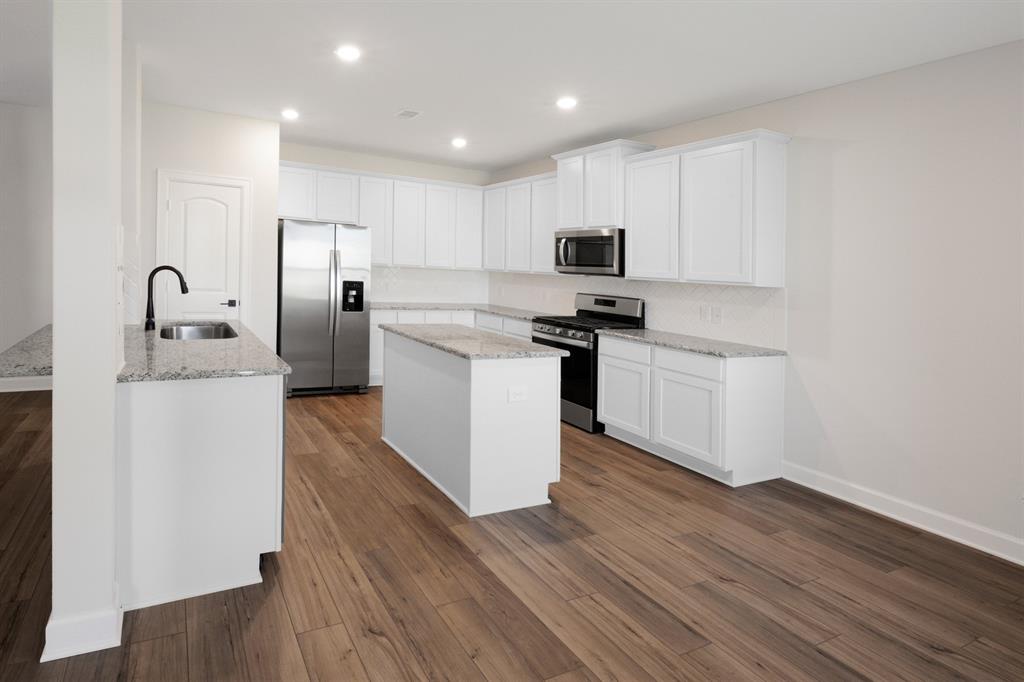 The combination of white cabinets, stainless steel appliances, and granite countertops infuses the kitchen with a bright and inviting ambiance, enhancing the sense of openness and freshness while reflecting natural light throughout the space.